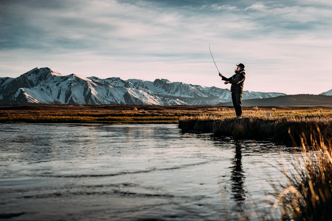 landscape-photo-of-man-fishing-on-river-near-mountain-alps-qr7tsswdog0